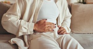 Woman, hands and stomach pain of menstruation on sofa with period cramps.
